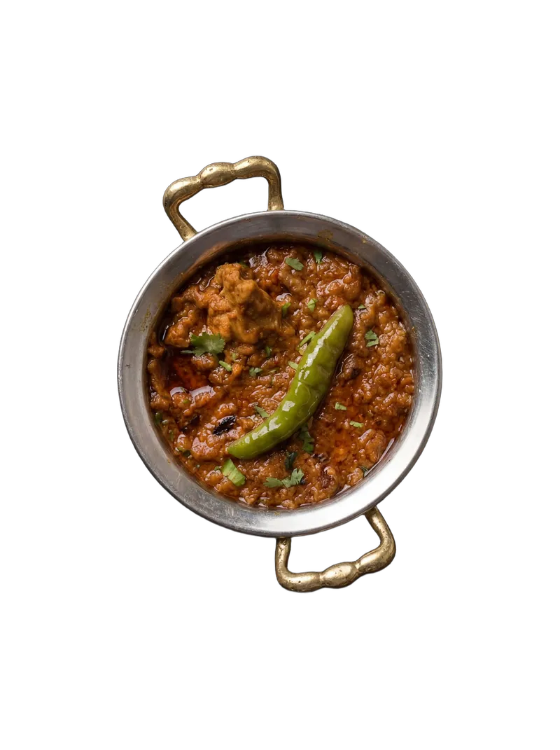 Mutton curry in a hammered brass-handled steel kadai with a whole green chili garnish