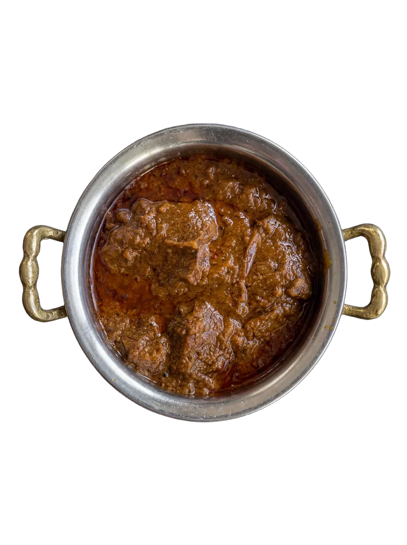 Kashmiri mutton rogan josh in a hammered brass-handled kadai with whole dried red chillies and fresh coriander