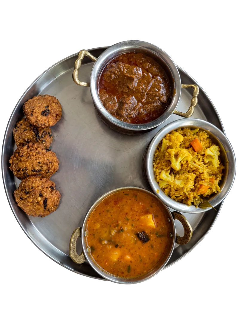 South Indian thali with 4 brass-handled steel katoris on a round steel tray, rotated for dynamism