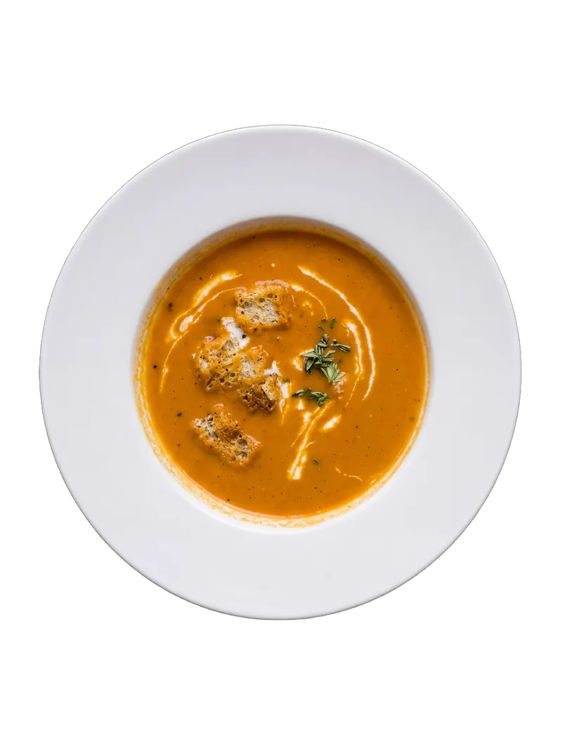 Tomato soup garnished with herb croutons in a white bowl